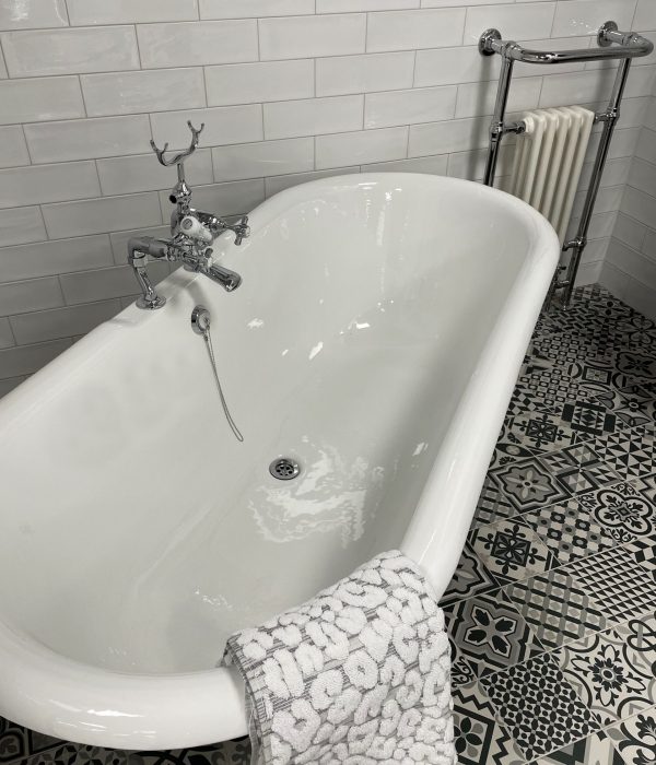 Stock photo showing luxury bathroom suite with Victorian style white ceramic, freestanding, curved roll top bath with metal claw feet, chrome, bath shower mixer tap and black and white patterned tiled flooring.