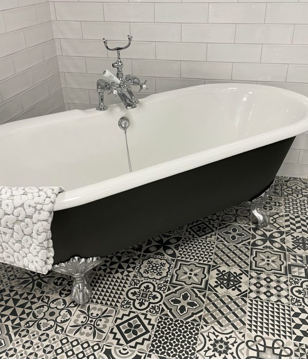 Stock photo showing luxury bathroom suite with Victorian style white ceramic, freestanding, curved roll top bath with metal claw feet, chrome, bath shower mixer tap and black and white patterned tiled flooring.