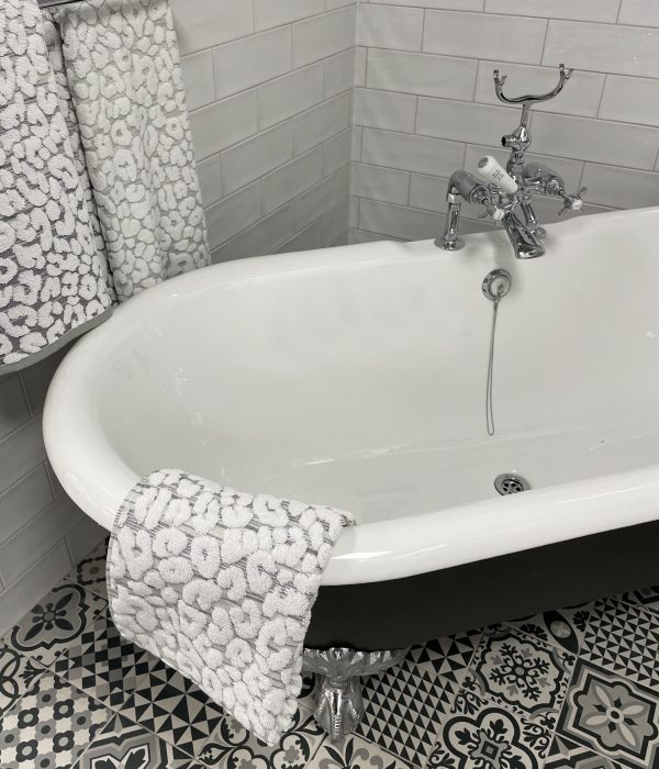 Stock photo showing luxury bathroom suite with Victorian style white ceramic, freestanding, curved roll top bath with metal claw feet, chrome, bath shower mixer tap and black and white patterned tiled flooring.