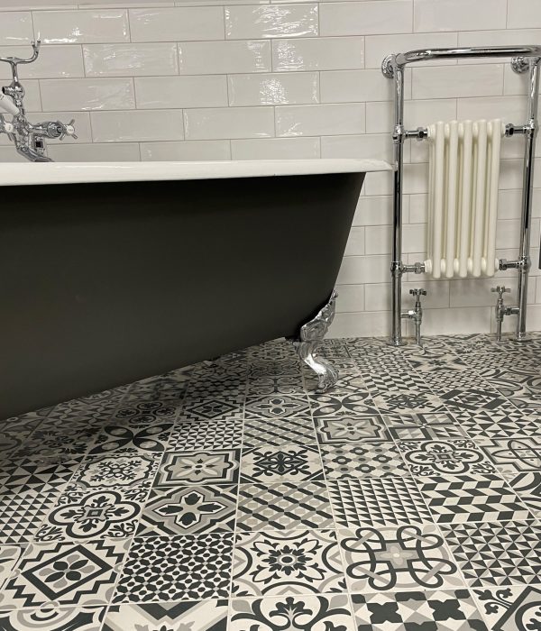 Stock photo showing luxury bathroom suite with Victorian style white ceramic, freestanding, curved roll top bath with metal claw feet, chrome, bath shower mixer tap and black and white patterned tiled flooring.
