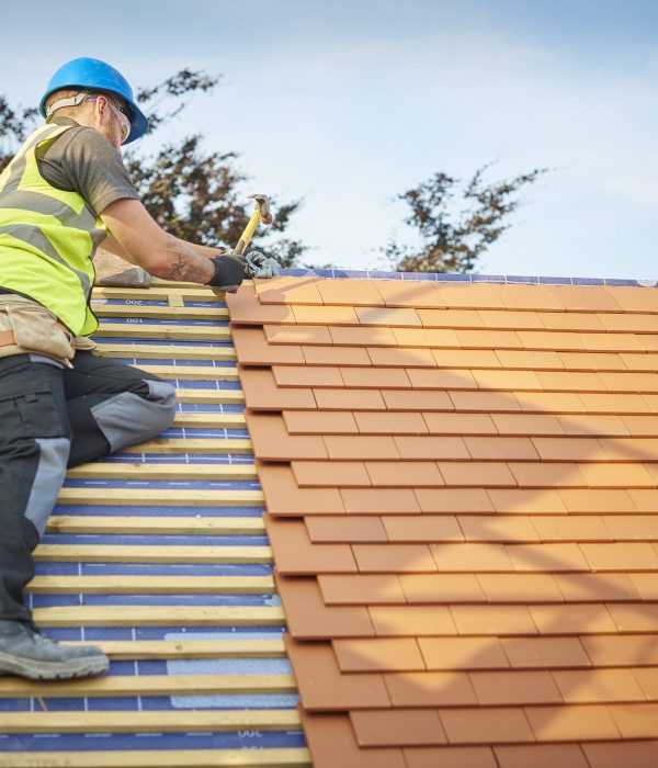 a roofer nails on the roof tiles
